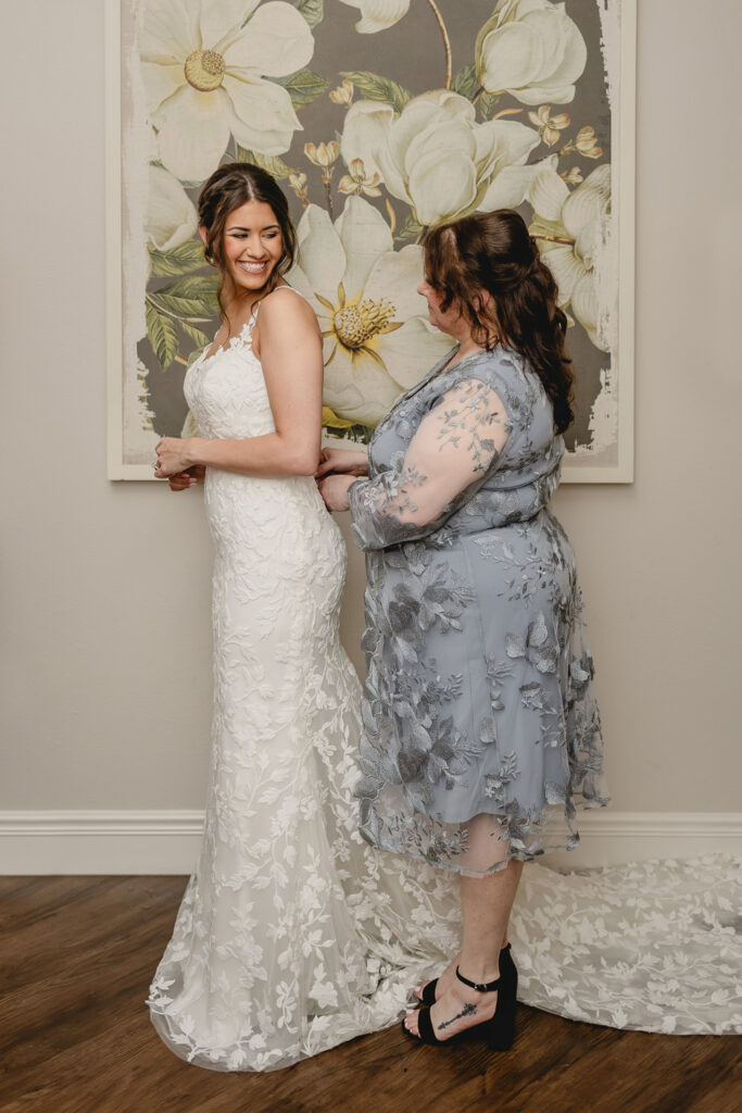 Mother of the bride zipping up her daughters dress in front of a flower painting