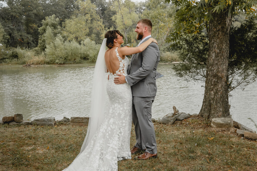 Bride and groom embrace each other during a first look at a lake front.