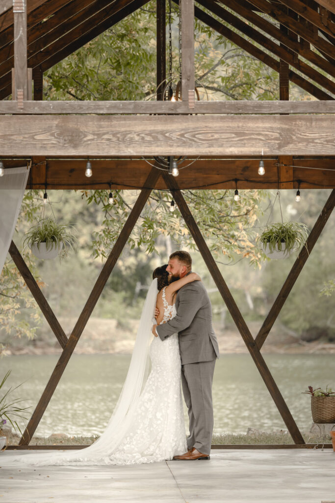 Bride and groom performing private vows in a lakeside gazebo hugging.