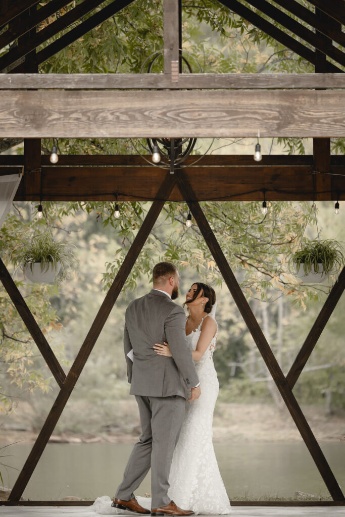 Bride and groom embrace while performing private vows in a lakeside gazebo