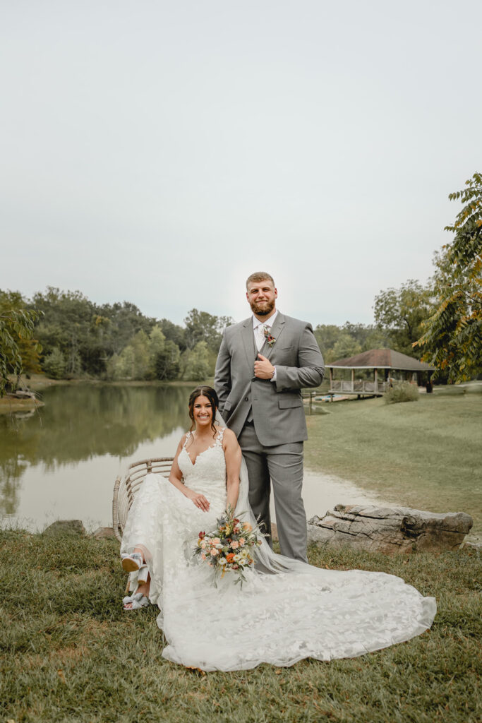 Bride and groom pose in a chair in front of lost hill lake.