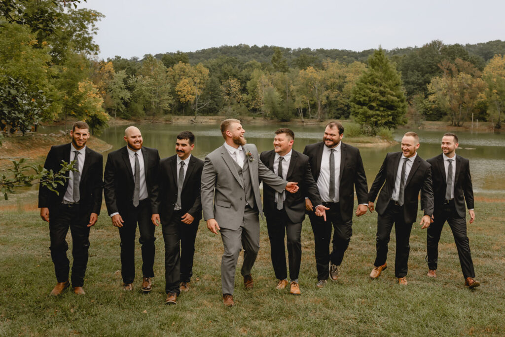 Groomsmen and groom laughing and walking along a lake.