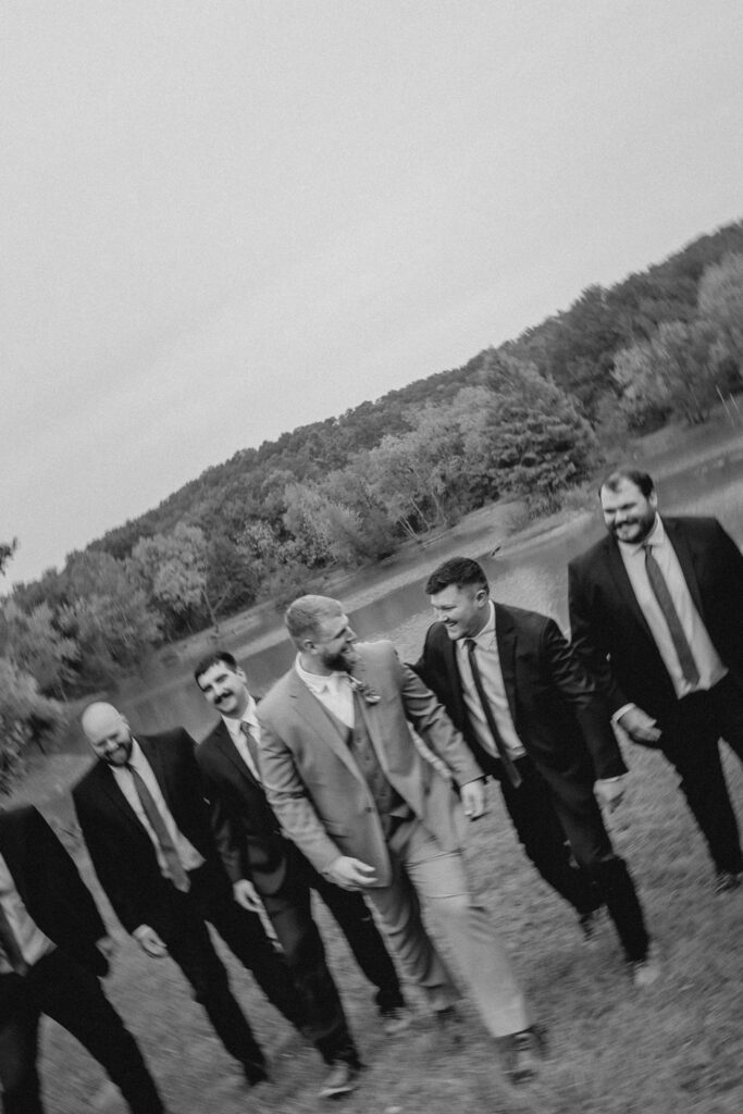 Groomsmen and groom laughing and walking along a lake.