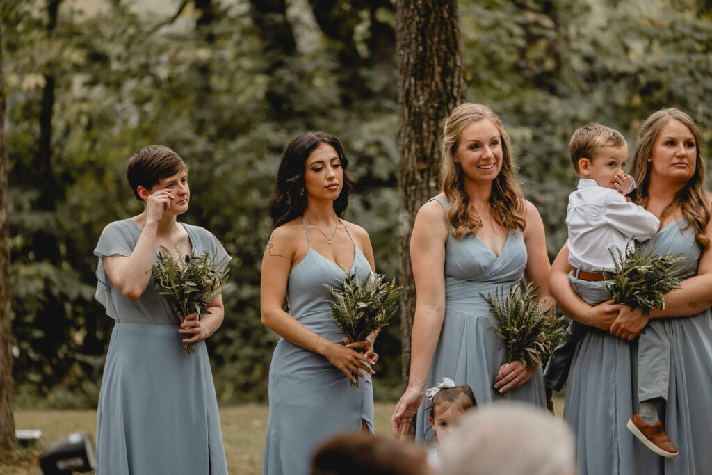 Bridesmaids in blue dress smiling during wedding ceremony.