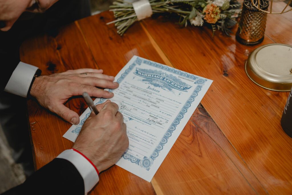 Marriage license being signed on natural wood table.