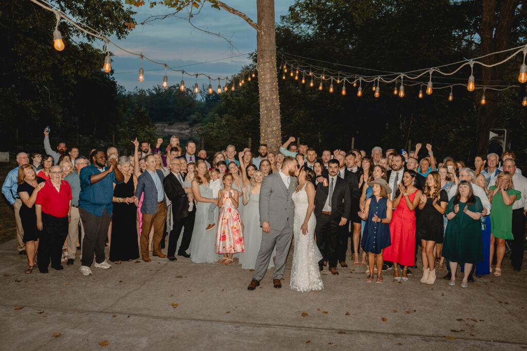 Whole wedding photo while bride and groom kiss in middle.