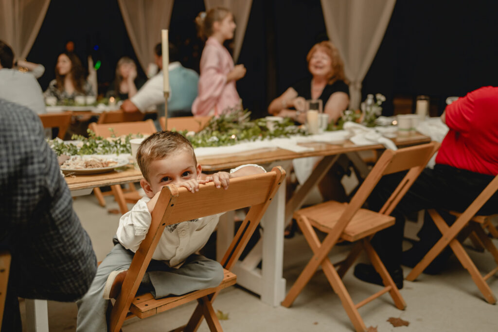Shy child hides behind his chair at wedding reception.