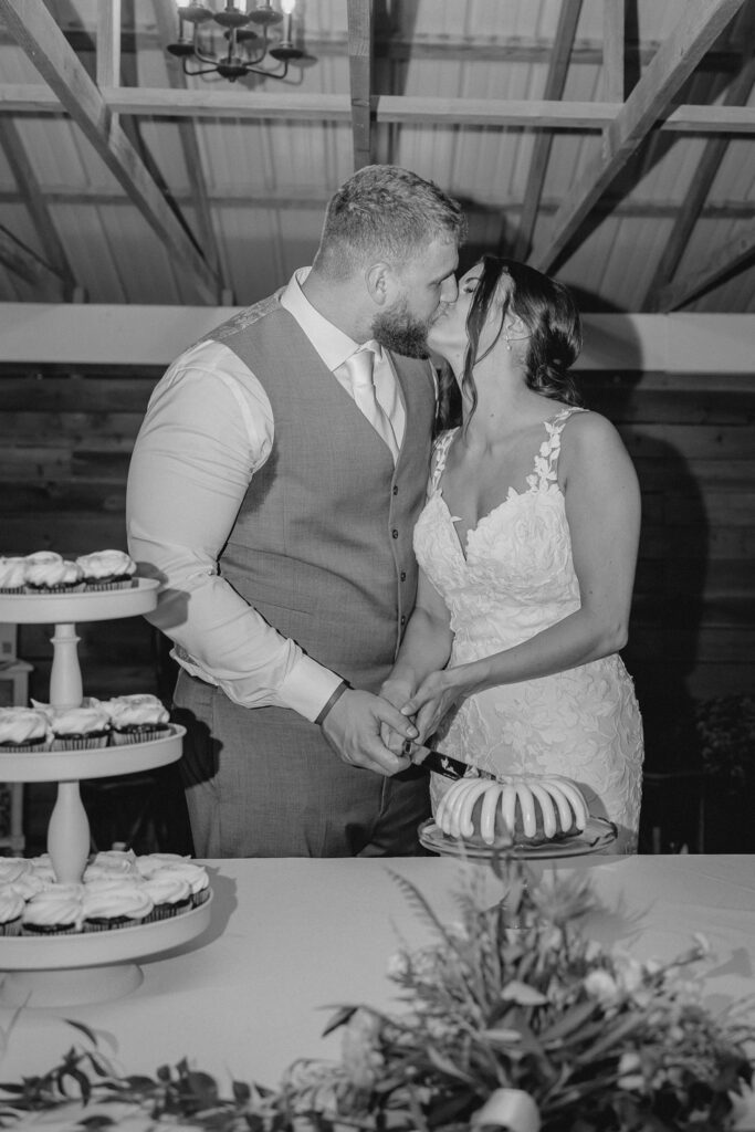 Bride and groom share a kiss while cutting cake at reception.