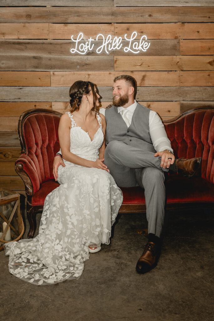 Bride and groom pose on a couch with a neon lost hill lake sign hanging on the wall.