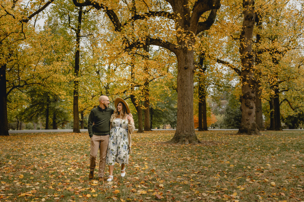 wide shot of a couple on the left side of the frame laughing and walking together through a peak fall park scene