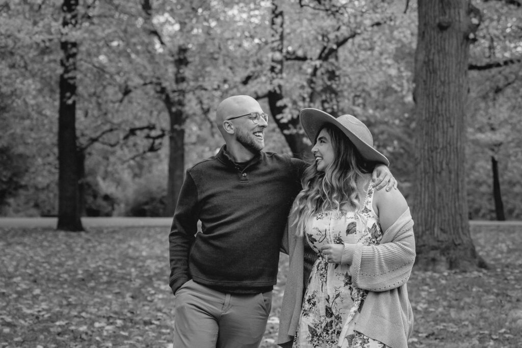 woman in floral dress, cardigan and fashion hat laughs with her classic sweatered boyfriend in a park 