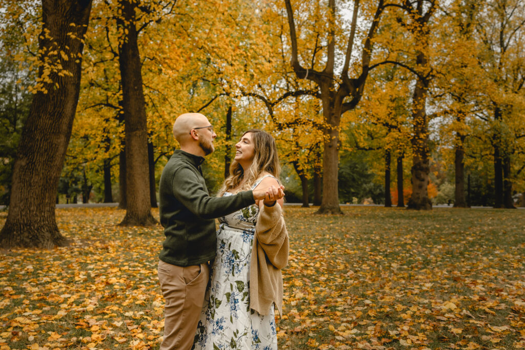 couple slow dancing in a park filled with yellow fall trees and fallen yellow leaves on the ground