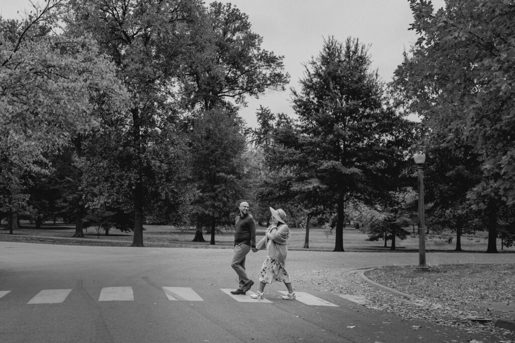 black and white side shot of a couple crossing the street in a park