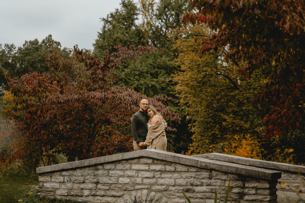 centered shot of a couple peacefully looking to the camera while embracing in the center of a romantic small stone bridge
