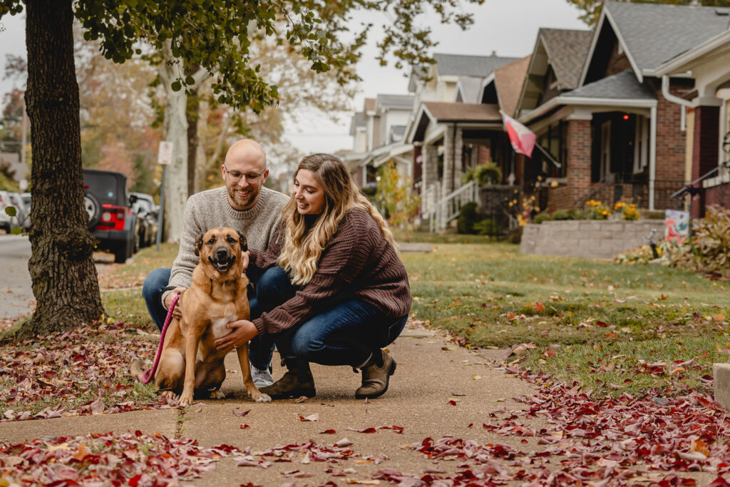 young couple stops mid-neighborhood walk to pet their smiling dog