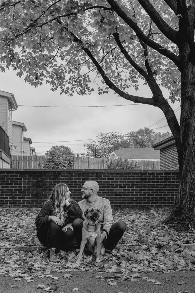 black and white of a young couple relaxing on a curb with their dog in a fall neighborhood scene
