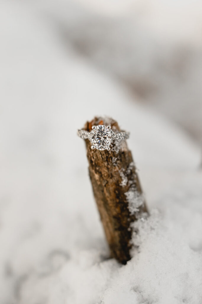 large oval diamond engagement ring perched on a stick peeking out of the snow