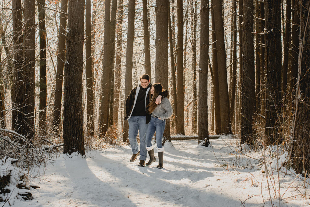  a young couple laugh and walk together through a snowy forest