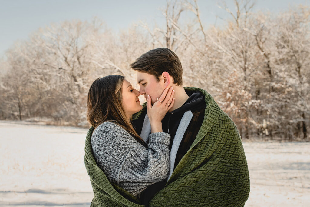 young woman holding her boyfriends cheek to pull him in close in front of a snow-covered landscape