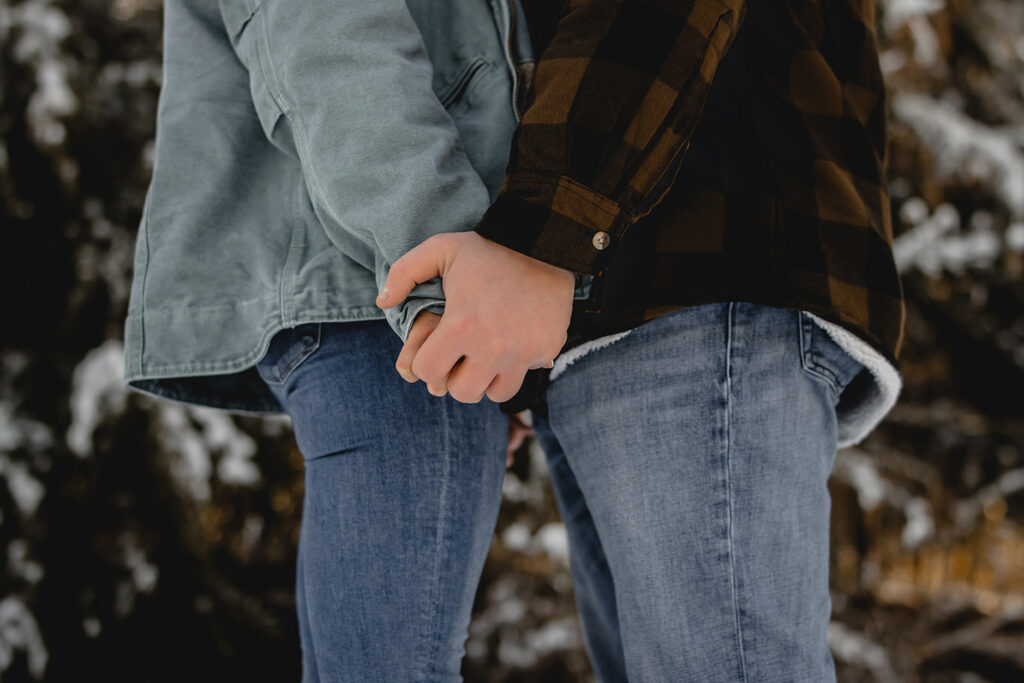 close up of a couple in jeans and winter jackets facing each other while holding hands