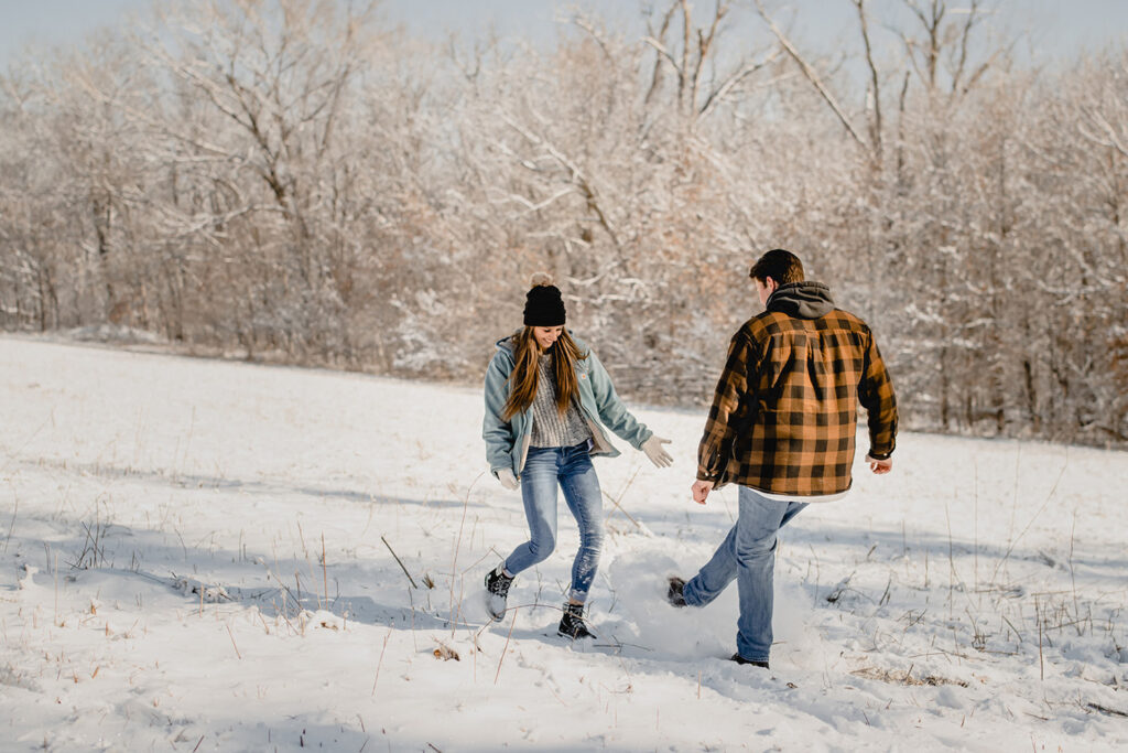 cute young couple playfully kick snow up towards each other in a large open snow meadow