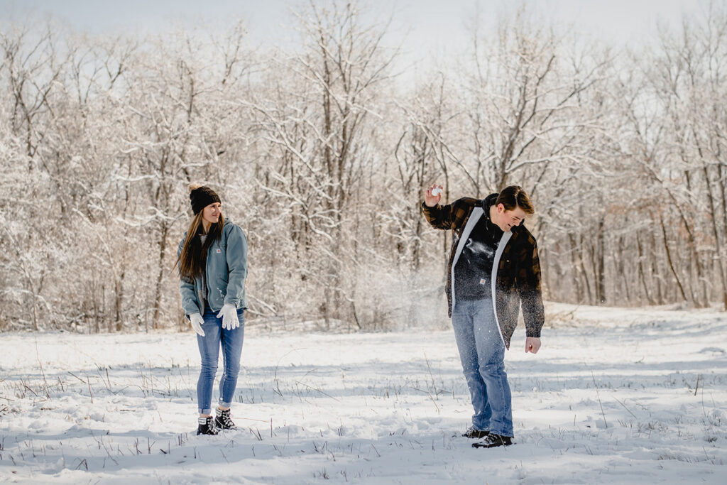 man laughing as the snowball his girlfriend has just thrown at him explodes on his side in a winter meadow