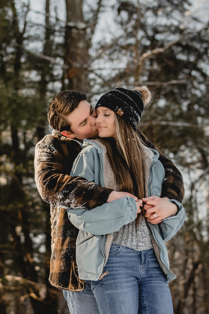 close up of man kissing his girlfriend's cheek as she smiles peacefully with her eyes closed, both dusted in snow