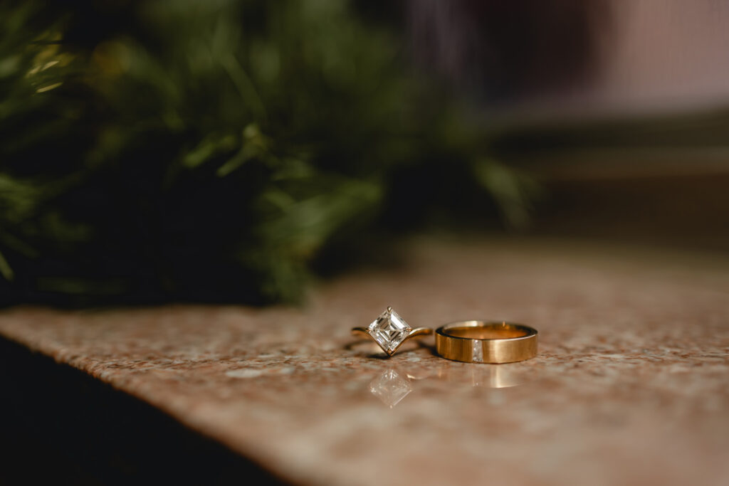 close up shot of 2 gold wedding rings sitting on reflective granite in front of green christmas garland