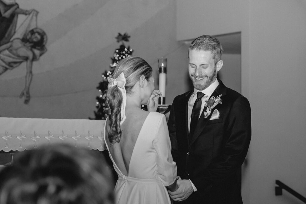 a young bride puts her hand to her mouth in laughter as the groom closes his eyes to giggle mid-ceremony