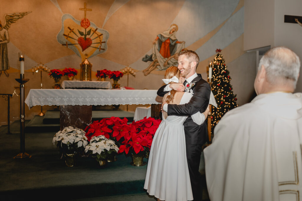 young newlyweds hug happily in a christmas-decorated church chapel after their first kiss upon being announced husband and wife