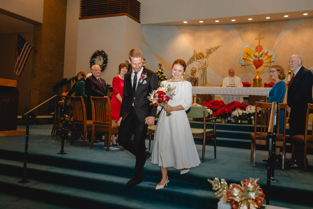 young newlyweds walk down carpeted church alter steps happily together after their ceremony